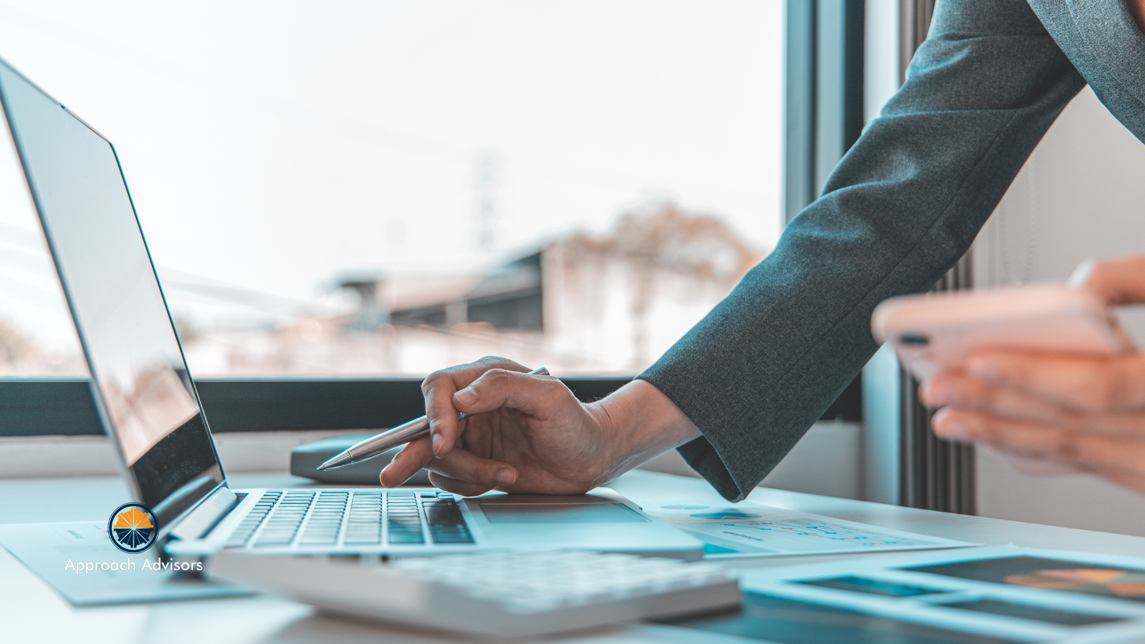 Business professional analyzing financial data on a laptop and smartphone, focusing on financial planning and business exit strategy.