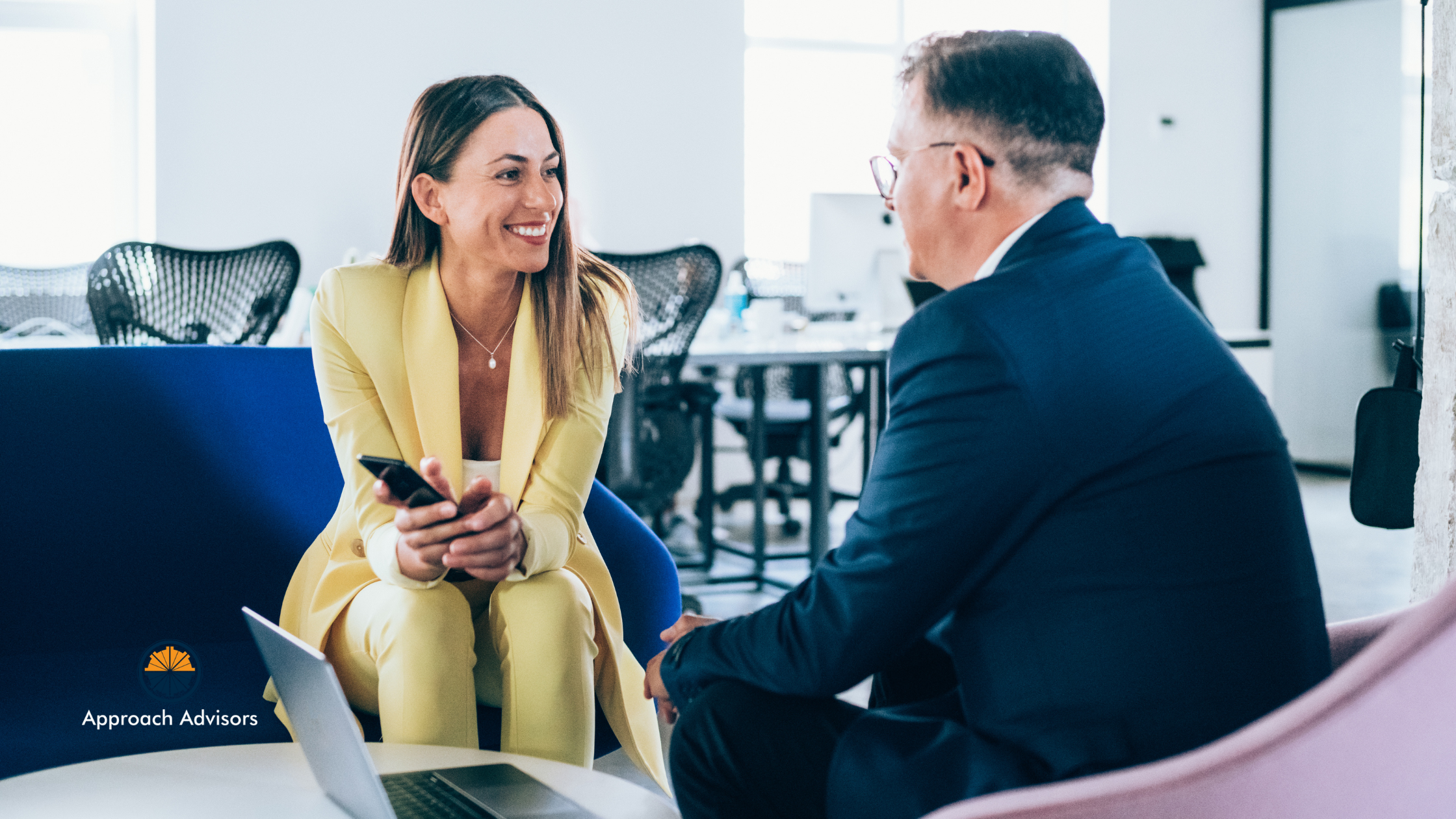Businesswoman in a yellow suit discussing financial planning and business exit strategy with a professional advisor in a modern office setting.