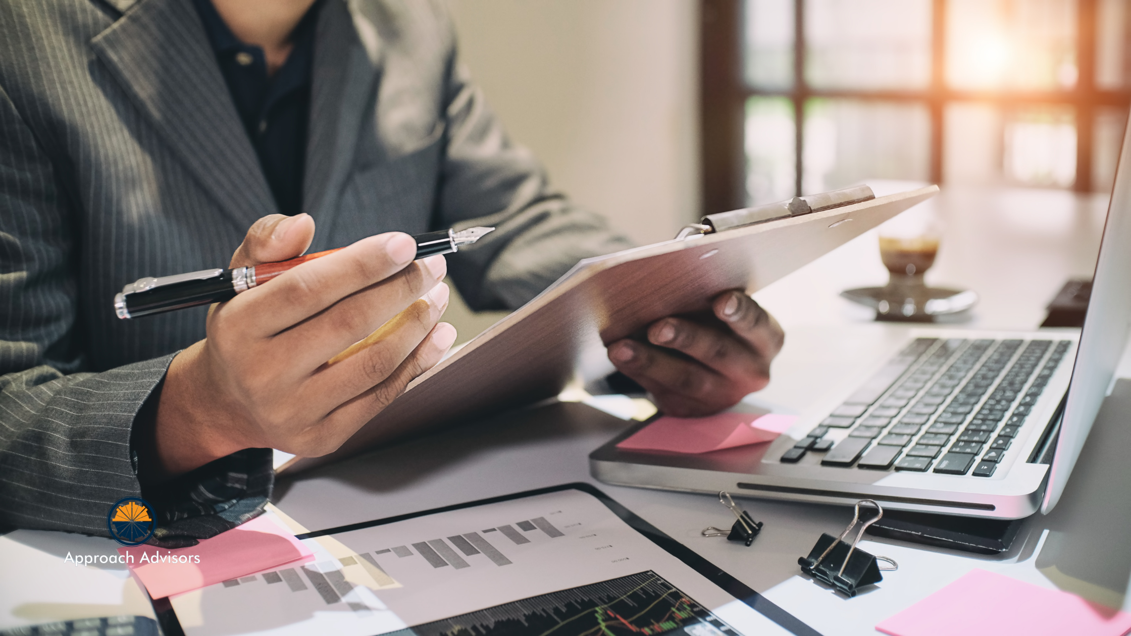 Business professional reviewing financial reports and charts on a clipboard and laptop during a content strategy analysis session.
